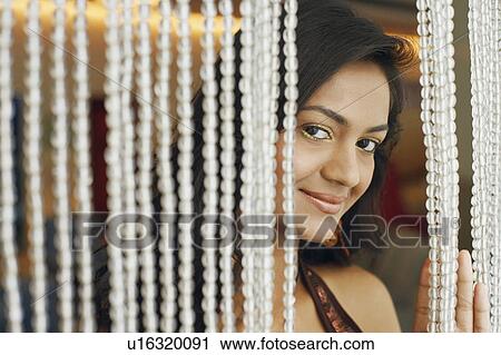 Stock Image - Portrait of a young woman smiling behind a beaded curtain. Fotosearch