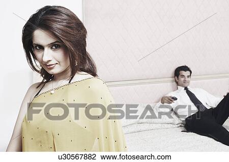Portrait of a young woman standing near a young man holding a remote control View Large Photo Image Stock Image - Portrait of a young woman standing near a young man holding a remote control. Fotosearch