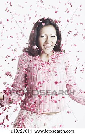 Stock Image - Portrait of a young woman standing with rose petals falling on her. Fotosearch