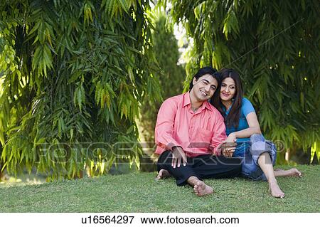 Stock Photo - Young couple sitting in a lawn and smiling. Fotosearch