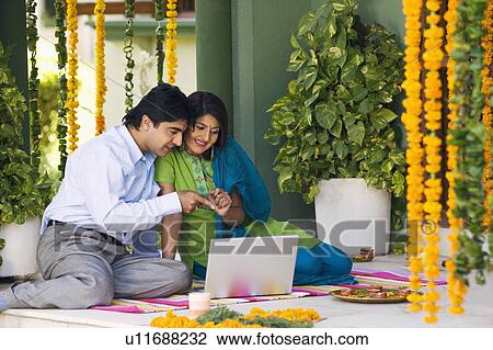 Young couple sitting on a mat and looking at a laptop View Large Photo Image Stock Image - Young couple sitting on a mat and looking at a laptop. Fotosearch