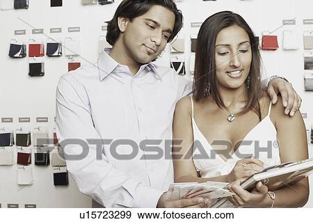 Stock Photo - Close-up of a young couple choosing fabric swatches from a magazine. Fotosearch