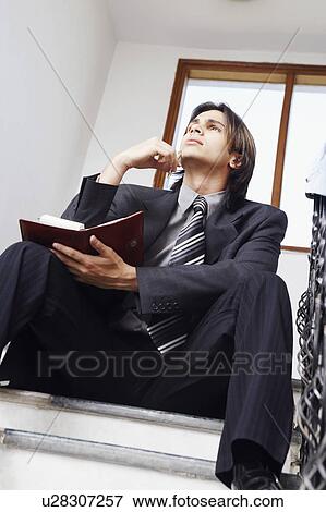 Low angle view of a businessman sitting on the staircase holding a personal organizer View Large Photo Image Stock Photo - Low angle view of a businessman sitting on the staircase holding a personal organizer. Fotosearch