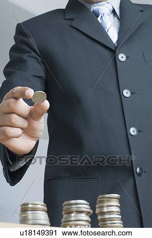 Stock Image - Mid section view of a businessman holding a coin. Fotosearch