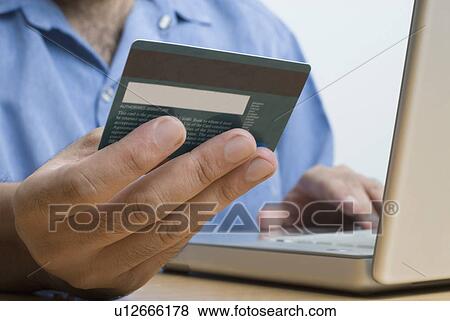 Stock Photo - Mid section view of a man holding a credit card and using a laptop. Fotosearch