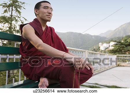 Picture - Monk sitting on the bench and holding prayer beads, McLeod Ganj, Dharmakot, Dharamshala, Himachal Pradesh, India. Fotosearch