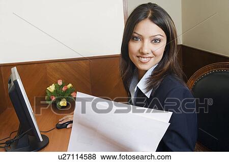 Portrait of a businesswoman working on a computer and holding a sheet of paper View Large Photo Image Stock Photo - Portrait of a businesswoman working on a computer and holding a sheet of paper. Fotosearch
