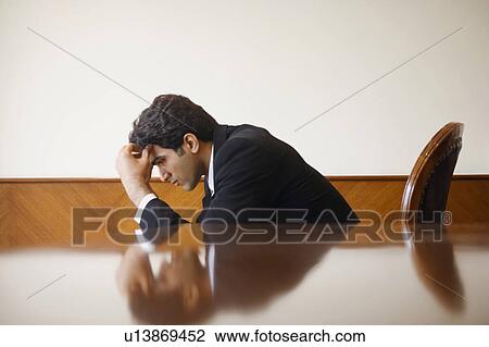 Stock Image - Side profile of a businessman sitting with his head in his hand. Fotosearch