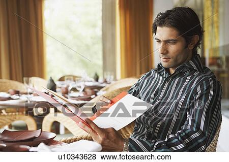 Young man sitting in a restaurant and reading a menu card View Large Photo Image Stock Photo - Young man sitting in a restaurant and reading a menu card. Fotosearch