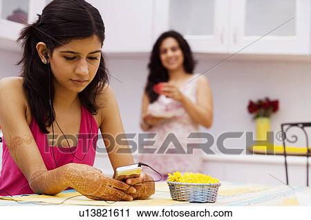 Young woman listening to music with a mid adult woman standing in the background View Large Photo Image Stock Image - Young woman listening to music with a mid adult woman standing in the background. Fotosearch