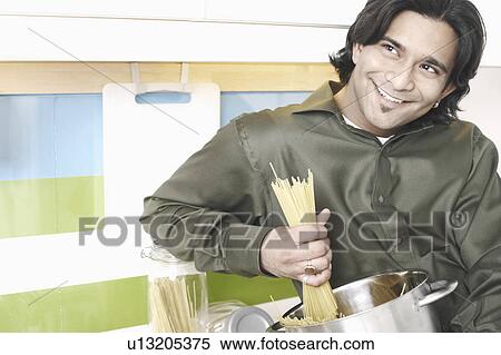 Stock Photography - Close-up of a young man cooking raw spaghetti. Fotosearch