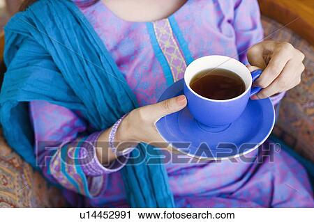 Stock Image - Mid section view of a woman holding a cup of tea. Fotosearch