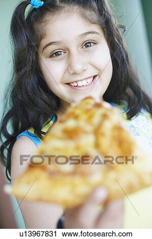 Stock Image - Portrait of a girl holding a slice of pizza. Fotosearch