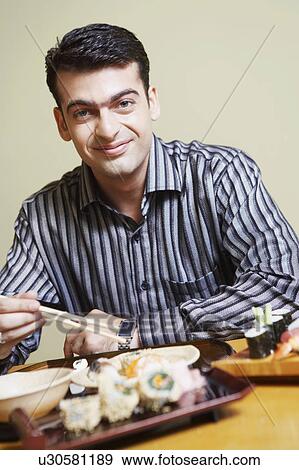 Stock Photo - Portrait of a young man sitting at the dining table and smirking. Fotosearch