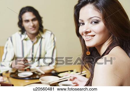 Stock Image - Portrait of a young woman sitting with a young man at the dining table and smiling. Fotosearch