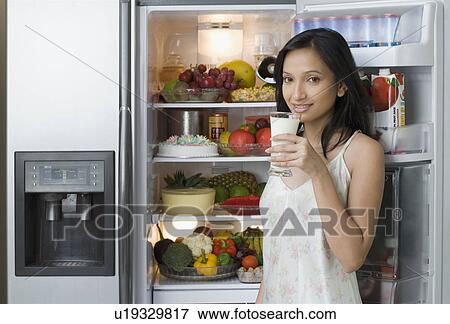 Stock Photo - Portrait of a young woman standing near a refrigerator and holding a glass of milk. Fotosearch