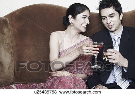 Stock Photo - Young couple toasting with martini and whiskey glasses. Fotosearch