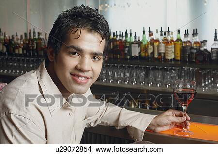 Portrait of a young man sitting at a bar counter and holding a glass of red wine View Large Photo Image Picture - Portrait of a young man sitting at a bar counter and holding a glass of red wine. Fotosearch