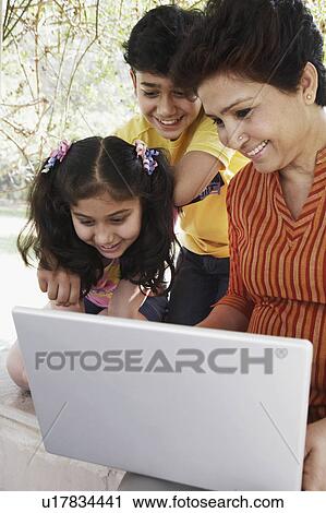 Stock Image - Close-up of a mature woman and her two grandchildren looking at a laptop. Fotosearch