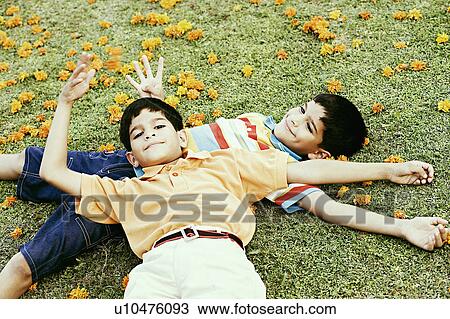 Stock Image - High angle view of a boy lying on the grass with his brother resting his head on his abdomen. Fotosearch