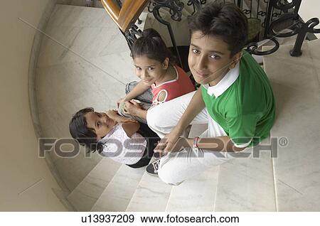 Stock Photo - High angle view of three children sitting on a staircase and smiling. Fotosearch
