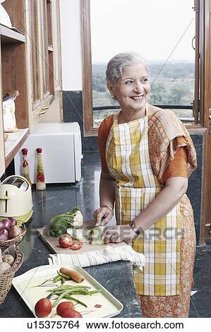 Picture - Mature woman cutting vegetables in the kitchen. Fotosearch