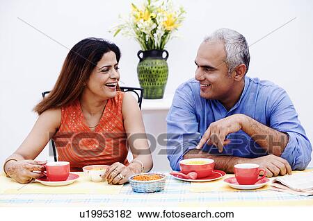 Mid adult couple sitting at the table and smiling View Large Photo Image Stock Image - Mid adult couple sitting at the table and smiling. Fotosearch