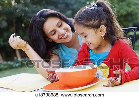 Stock Photography - Mid adult woman with her daughter sitting at a table and smiling. Fotosearch