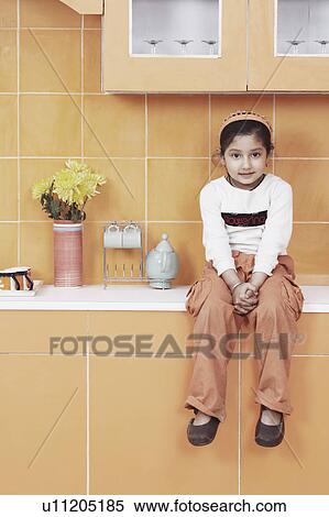 Stock Photography - Portrait of a girl sitting on a kitchen counter. Fotosearch