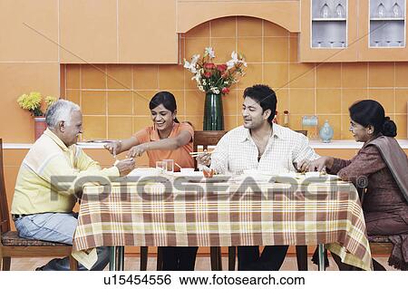 Stock Photograph - Side profile of a mature couple and their two children at the dining table. Fotosearch