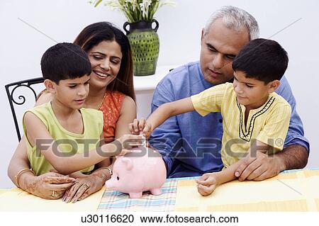 Two boys inserting Indian currency notes into a piggy bank with their parents sitting beside them View Large Photo Image Stock Image - Two boys inserting Indian currency notes into a piggy bank with their parents sitting beside them. Fotosearch
