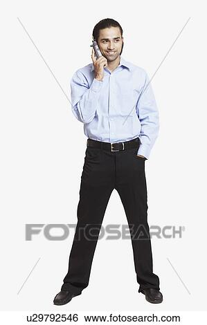 Close-up of a young man standing and talking on a mobile phone View Large Photo Image Stock Photograph - Close-up of a young man standing and talking on a mobile phone. Fotosearch