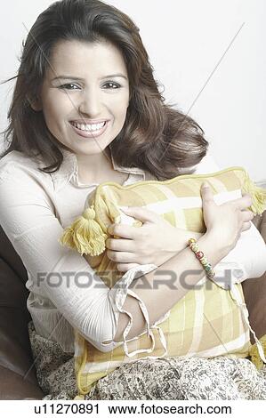 Stock Image - Portrait of a young woman hugging a cushion. Fotosearch
