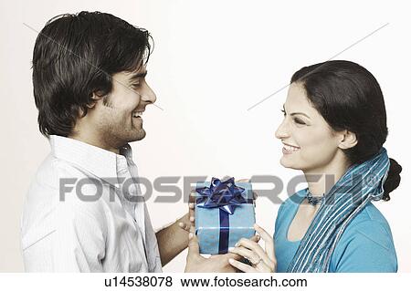 Stock Photo - Side profile of a young couple holding a gift box. Fotosearch