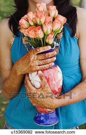 Stock Image - Mid section view of a young woman holding a vase of Roses. Fotosearch