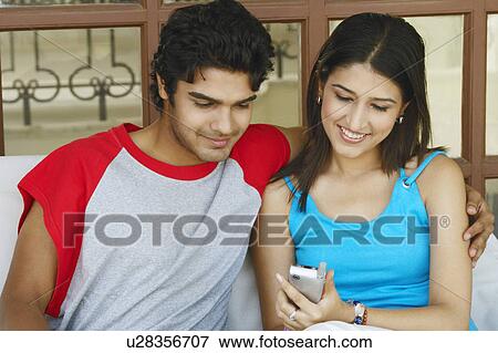 Stock Photo - Close-up of a young couple sitting together holding a mobile phone. Fotosearch