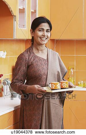 Stock Photo - Portrait of a mature woman holding a tray with two cups. Fotosearch