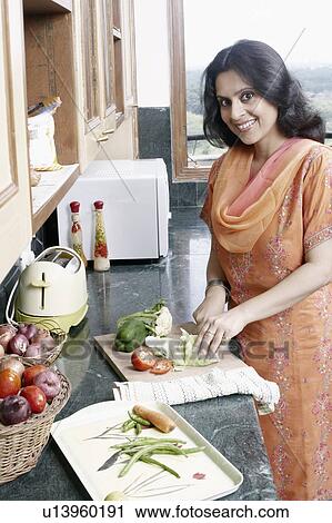 Stock Image - Portrait of a mid adult woman cutting vegetables in the kitchen. Fotosearch
