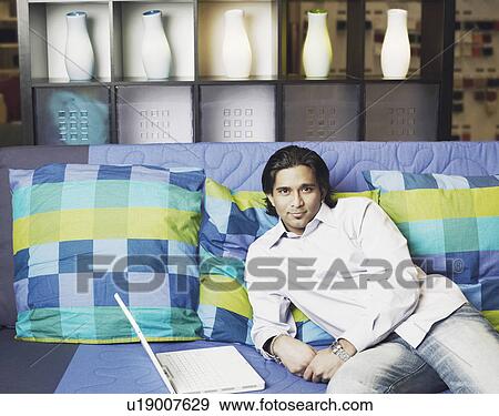 Stock Photo - Portrait of a young man lying on the couch with a laptop. Fotosearch