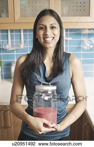 Stock Image - Portrait of a young woman holding a jar of chilli powder. Fotosearch