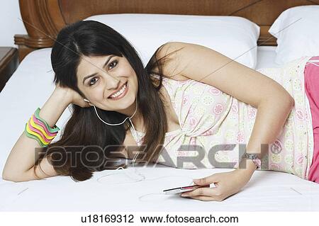 Stock Image - Portrait of a young woman lying on the bed and listening to music. Fotosearch