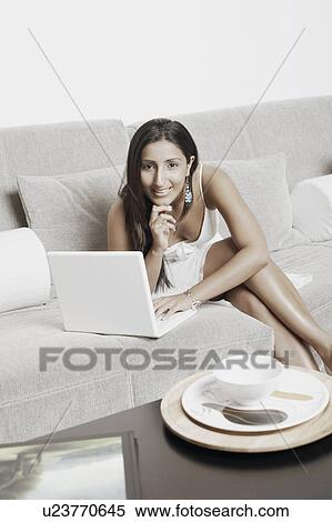 Stock Photography - Portrait of a young woman sitting in front of a laptop with her hand on her chin. Fotosearch