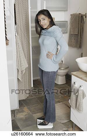 Picture - Portrait of a young woman standing on a weighing scale. Fotosearch