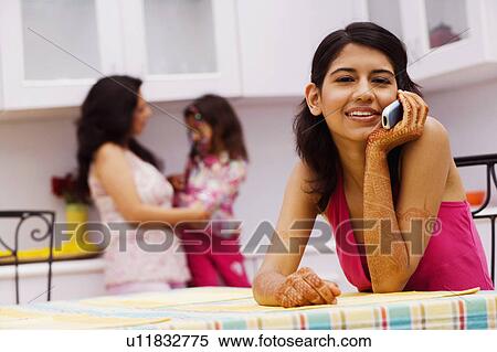 Portrait of a young woman talking on a mobile phone and a mid adult woman standing with her daughter in the background View Large Photo Image Stock Photography - Portrait of a young woman talking on a mobile phone and a mid adult woman standing with her daughter in the background. Fotosearch