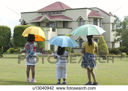 Rear view of three girls holding umbrellas and standing in a lawn View Large Photo Image Stock Image - Rear view of three girls holding umbrellas and standing in a lawn. Fotosearch