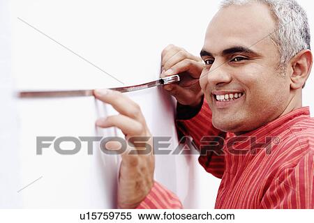Stock Photography - Side profile of a mid adult man measuring a wall with a measuring tape. Fotosearch