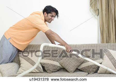 Stock Photo - Side profile of a young man cleaning a couch with a vacuum cleaner. Fotosearch