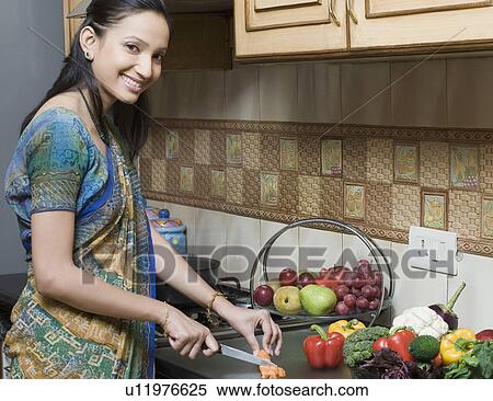 Stock Photography - Side profile of a young woman cutting vegetables in the kitchen. Fotosearch
