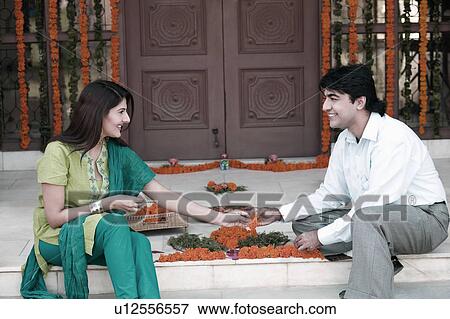 Stock Photo - Young couple sitting and decorating doorstep of a house with flowers. Fotosearch