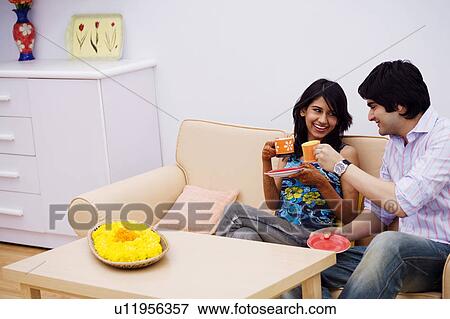 Stock Photo - Young couple sitting on a couch and holding cups of tea. Fotosearch